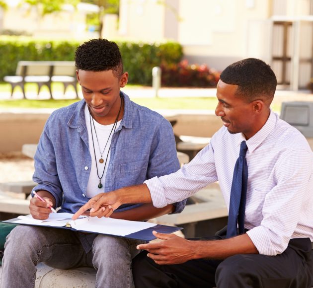 Teacher,Sitting,Outdoors,Helping,Male,Student,With,Work